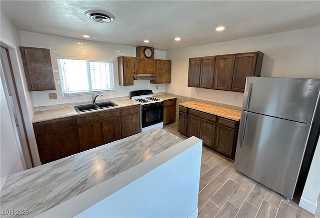 kitchen featuring visible vents, freestanding refrigerator, gas range oven, under cabinet range hood, and a sink