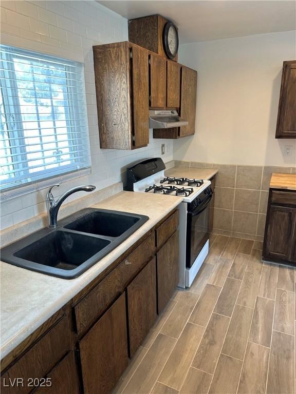 kitchen featuring tile walls, range hood, light countertops, gas range oven, and a sink