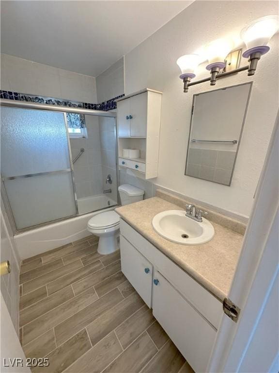 full bathroom with vanity, bath / shower combo with glass door, wood finish floors, and toilet