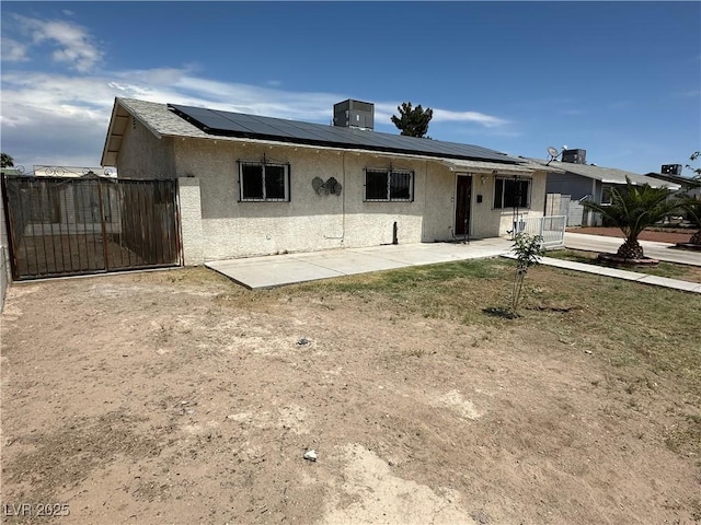 view of front facade with solar panels, a gate, a patio area, and stucco siding