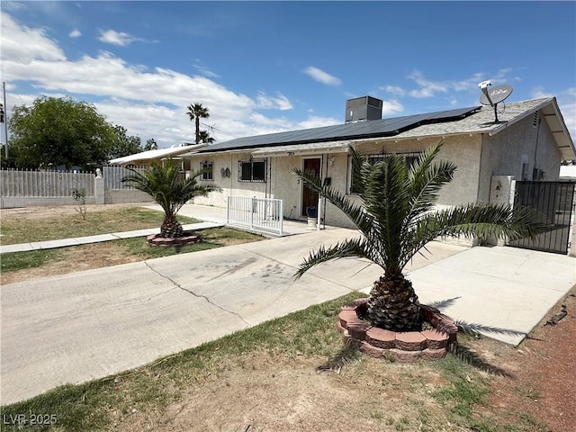 view of front of house featuring a gate, a fenced front yard, roof mounted solar panels, and stucco siding