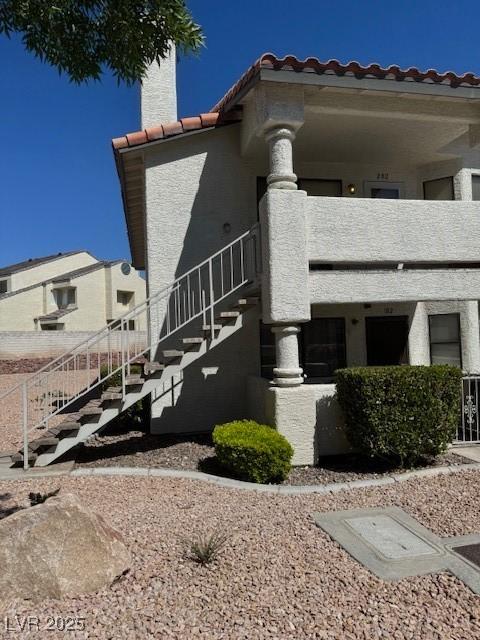 view of side of home featuring stairway, stucco siding, a tile roof, and a balcony