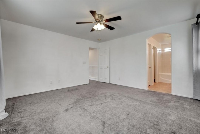 unfurnished room featuring carpet floors, arched walkways, a ceiling fan, and baseboards