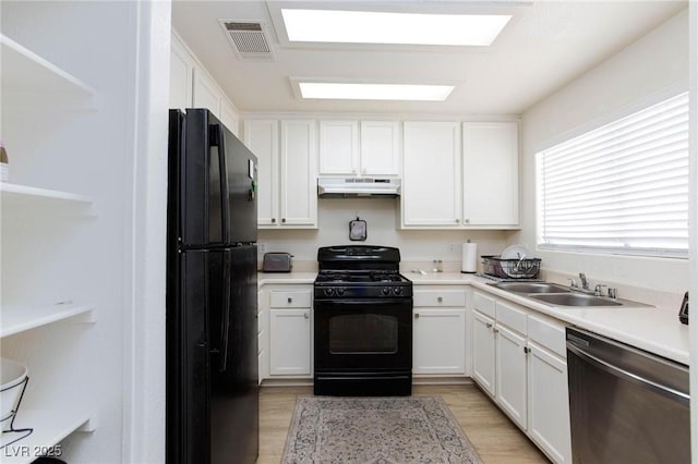 kitchen with light wood finished floors, a sink, visible vents, black appliances, and under cabinet range hood
