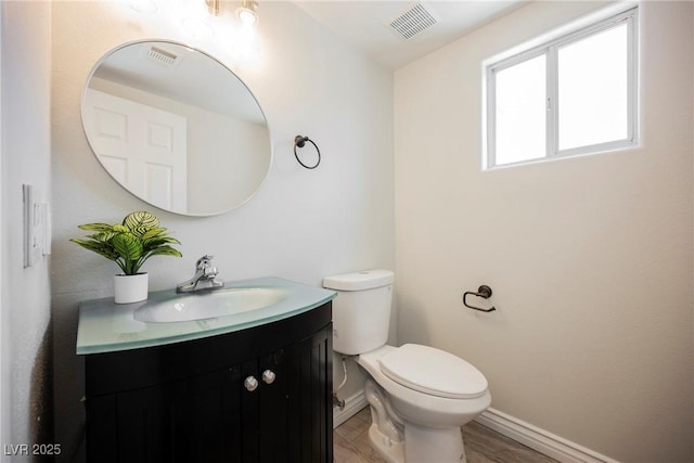 half bathroom featuring baseboards, visible vents, toilet, and vanity