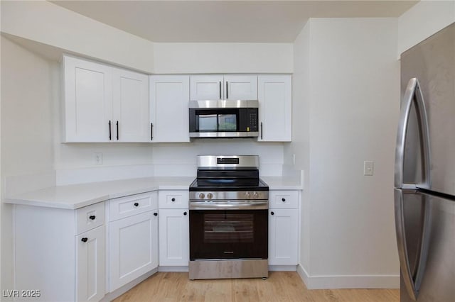 kitchen featuring appliances with stainless steel finishes, light countertops, light wood-style flooring, white cabinetry, and baseboards