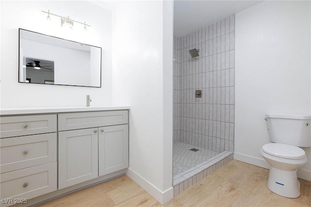 bathroom with a ceiling fan, a tile shower, wood finished floors, vanity, and toilet