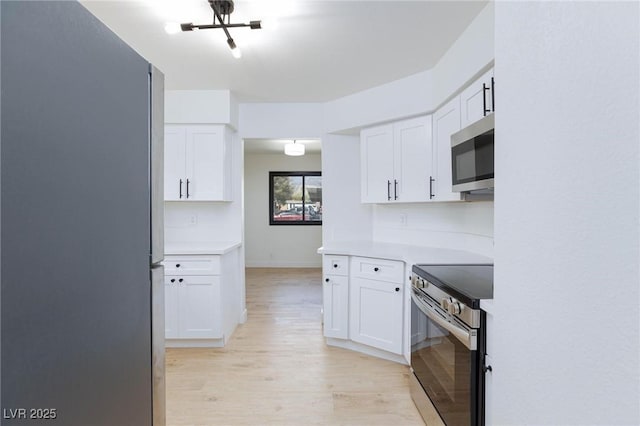 kitchen with appliances with stainless steel finishes, light countertops, light wood-style flooring, white cabinetry, and baseboards