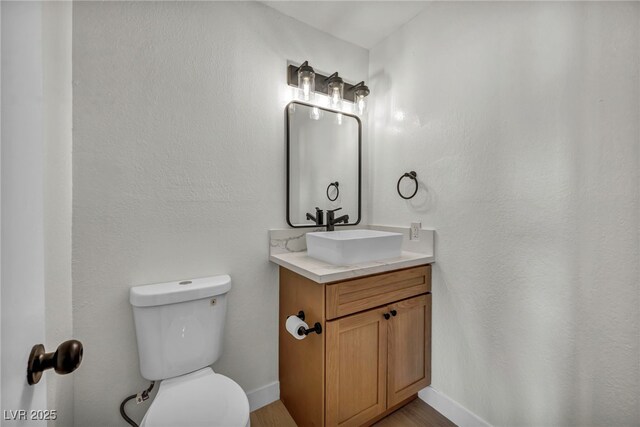 half bath featuring toilet, baseboards, wood finished floors, and vanity