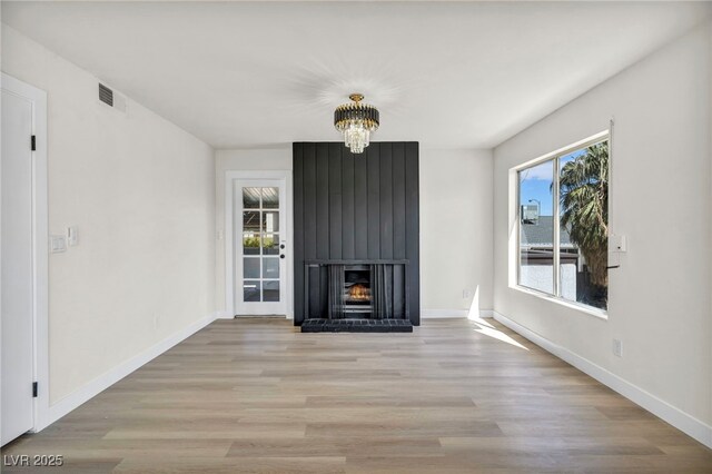 unfurnished living room with a notable chandelier, light wood-style floors, a large fireplace, baseboards, and visible vents