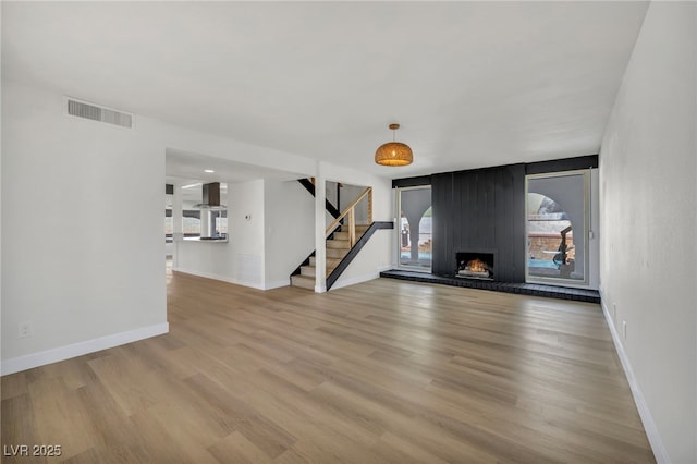 unfurnished living room featuring visible vents, a fireplace, wood finished floors, baseboards, and stairs