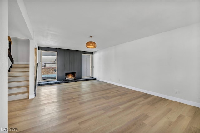 unfurnished living room with baseboards, light wood finished floors, stairway, and a large fireplace