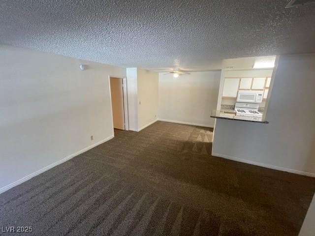 unfurnished room featuring baseboards, ceiling fan, dark colored carpet, and a textured ceiling