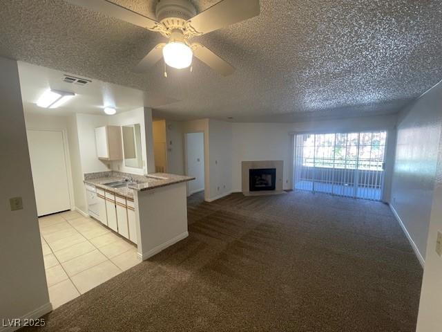kitchen with a textured ceiling, visible vents, baseboards, light carpet, and white cabinetry