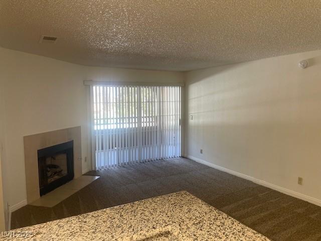 unfurnished living room featuring a textured ceiling, a fireplace with flush hearth, baseboards, and carpet