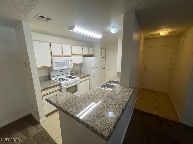 kitchen with a sink, white appliances, a peninsula, light tile patterned floors, and visible vents