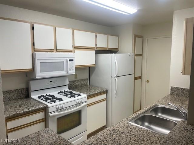 kitchen with white appliances, white cabinets, stone countertops, and a sink