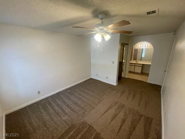 empty room with ceiling fan, carpet floors, arched walkways, a textured ceiling, and visible vents