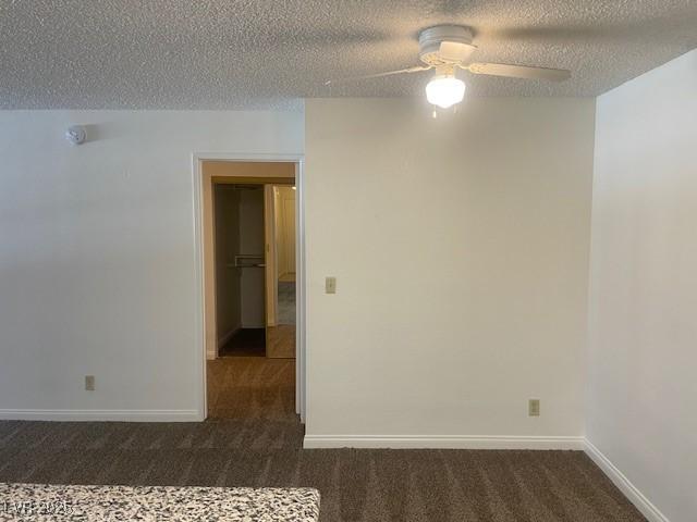 empty room featuring dark carpet, a ceiling fan, and a textured ceiling