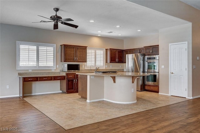kitchen featuring light stone counters, light wood-style floors, stainless steel appliances, a kitchen bar, and a kitchen island