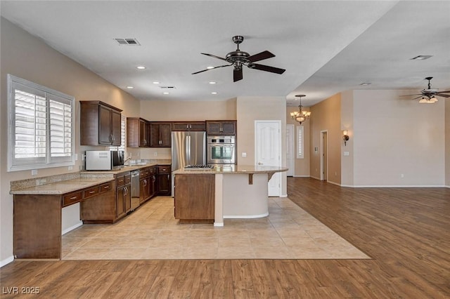 kitchen with visible vents, appliances with stainless steel finishes, a center island, ceiling fan with notable chandelier, and light wood finished floors