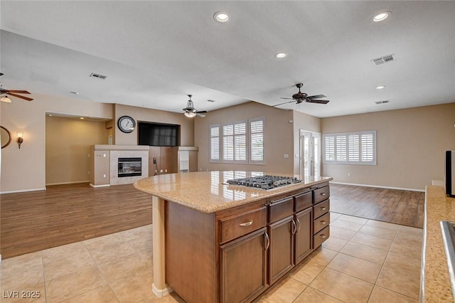 kitchen featuring a ceiling fan, stainless steel gas cooktop, open floor plan, and a fireplace