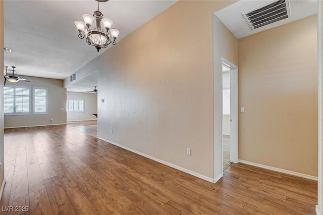 spare room with an inviting chandelier, baseboards, hardwood / wood-style flooring, and visible vents
