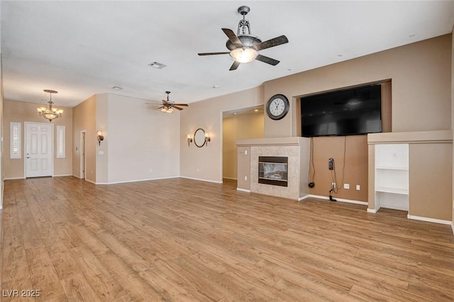 unfurnished living room with light wood-style flooring, ceiling fan with notable chandelier, baseboards, a tile fireplace, and visible vents