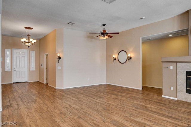 unfurnished living room with visible vents, wood finished floors, baseboards, a tiled fireplace, and ceiling fan with notable chandelier