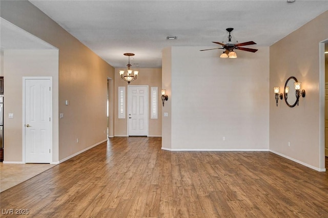 unfurnished living room featuring baseboards, ceiling fan with notable chandelier, and wood finished floors