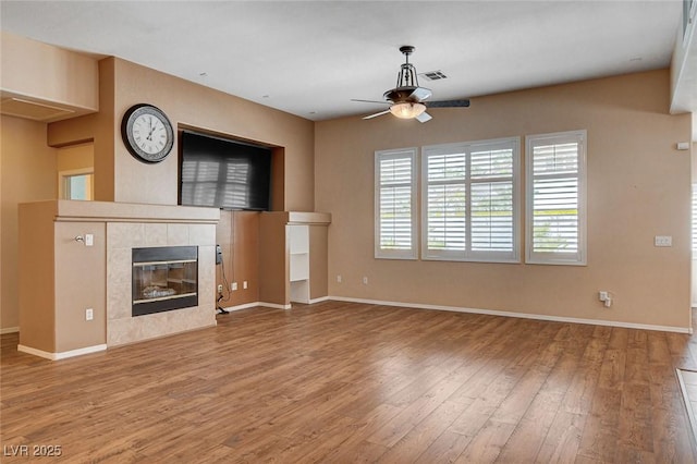 unfurnished living room with visible vents, wood finished floors, a fireplace, baseboards, and a ceiling fan