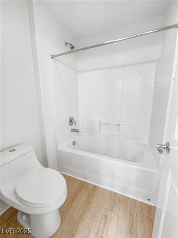 full bath with bathing tub / shower combination, toilet, and wood finished floors