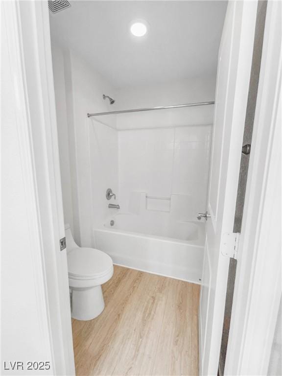 bathroom with wood finished floors, bathing tub / shower combination, and toilet