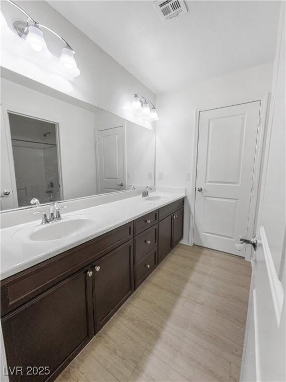 bathroom with double vanity, visible vents, a sink, and wood finished floors