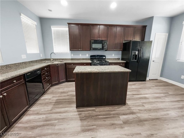 kitchen with dark brown cabinets, a sink, light wood-style floors, a center island, and black appliances
