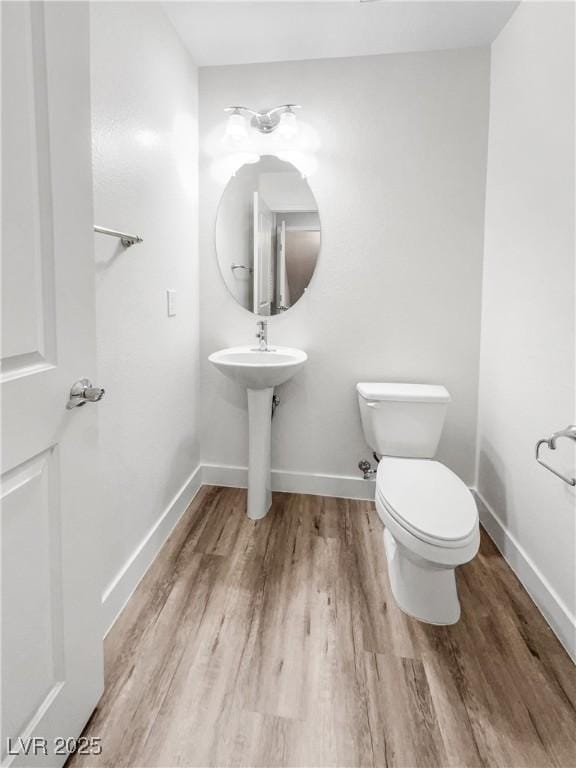 half bathroom with toilet, baseboards, and wood finished floors