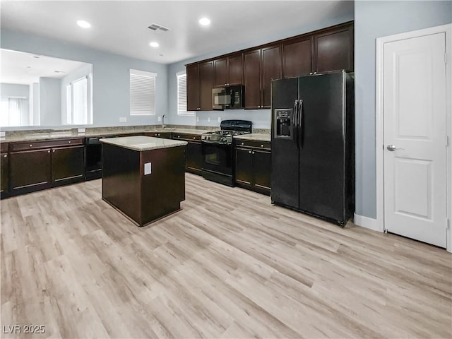 kitchen featuring a sink, light wood-type flooring, a kitchen island, visible vents, and black appliances