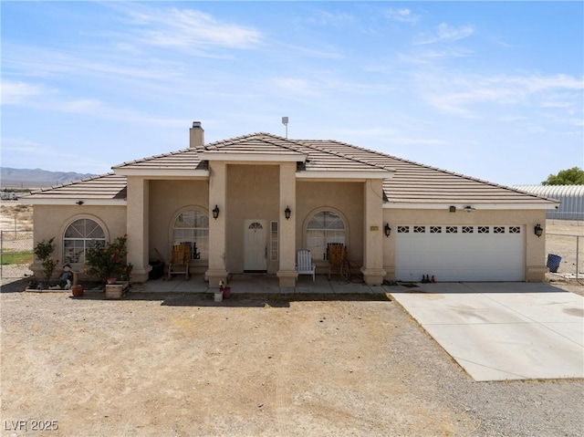 view of front facade with a tiled roof, a chimney, concrete driveway, an attached garage, and stucco siding