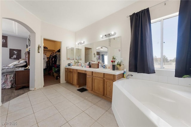 bathroom with a garden tub, double vanity, tile patterned flooring, a spacious closet, and a sink
