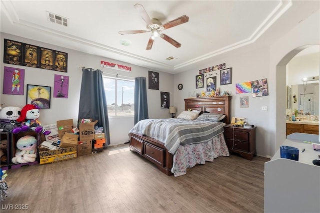 bedroom featuring arched walkways, visible vents, wood finished floors, and a raised ceiling