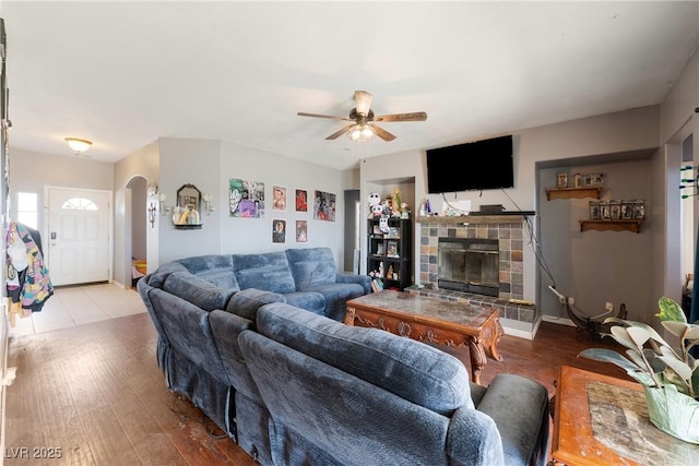 living area with arched walkways, ceiling fan, a tile fireplace, and wood finished floors