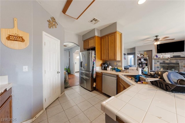 kitchen with visible vents, dishwashing machine, stainless steel fridge, tile countertops, and arched walkways