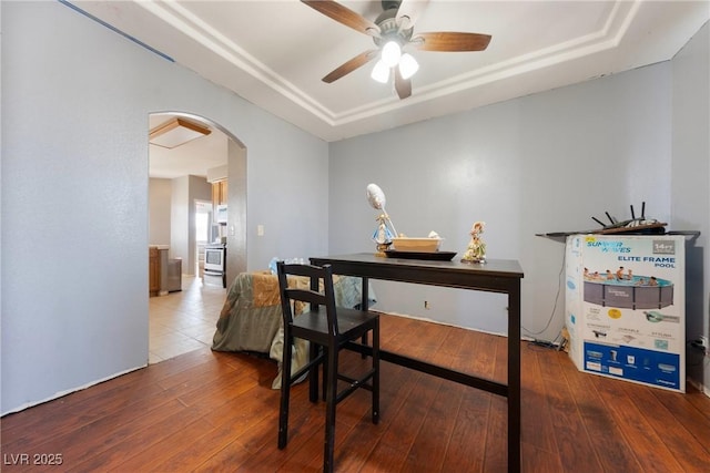 office with arched walkways, a raised ceiling, a ceiling fan, and hardwood / wood-style floors