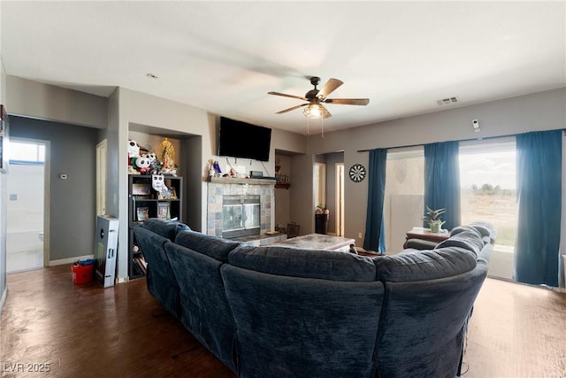 living room featuring a stone fireplace, ceiling fan, wood finished floors, and visible vents
