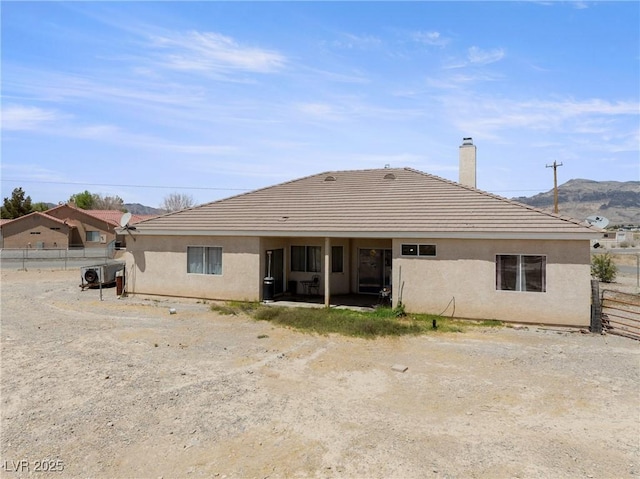 back of property with a mountain view, stucco siding, a chimney, and fence