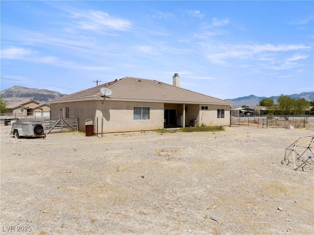 rear view of property featuring stucco siding, a mountain view, a tile roof, and fence