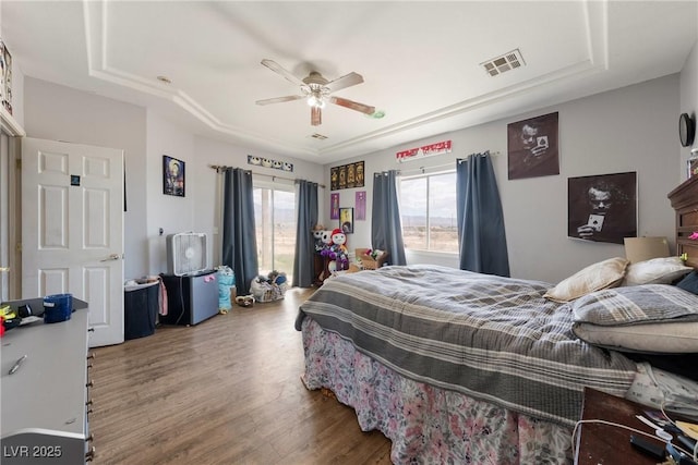 bedroom with a raised ceiling, a ceiling fan, wood finished floors, and visible vents