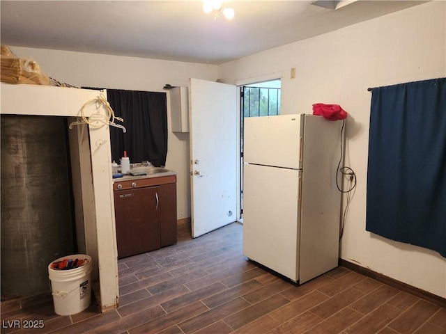 kitchen featuring freestanding refrigerator, dark wood-style flooring, baseboards, light countertops, and a sink