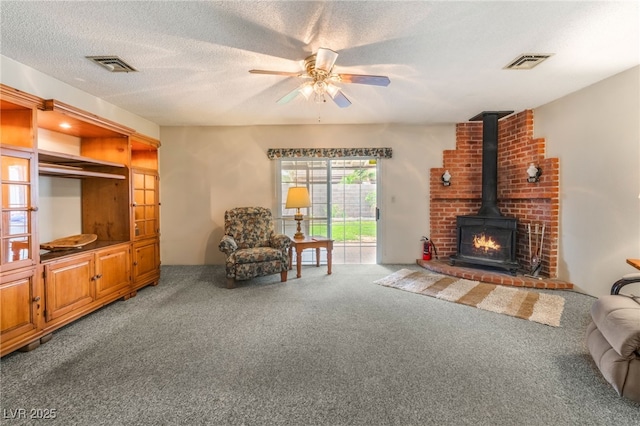 carpeted living room with visible vents, a wood stove, a textured ceiling, and ceiling fan