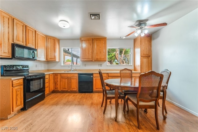 kitchen featuring a healthy amount of sunlight, a sink, black appliances, and light wood-style floors